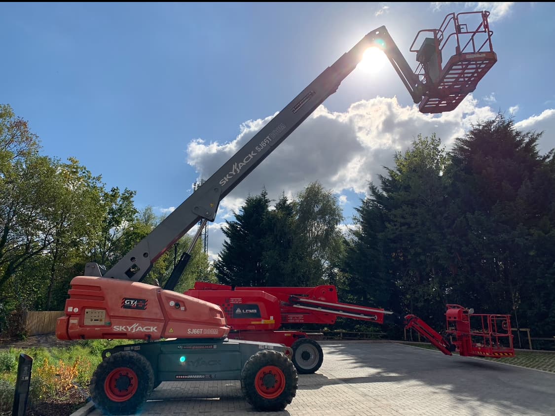 Skyjack SJ66T articulated boom lift fully extended against a blue sky, basket at height