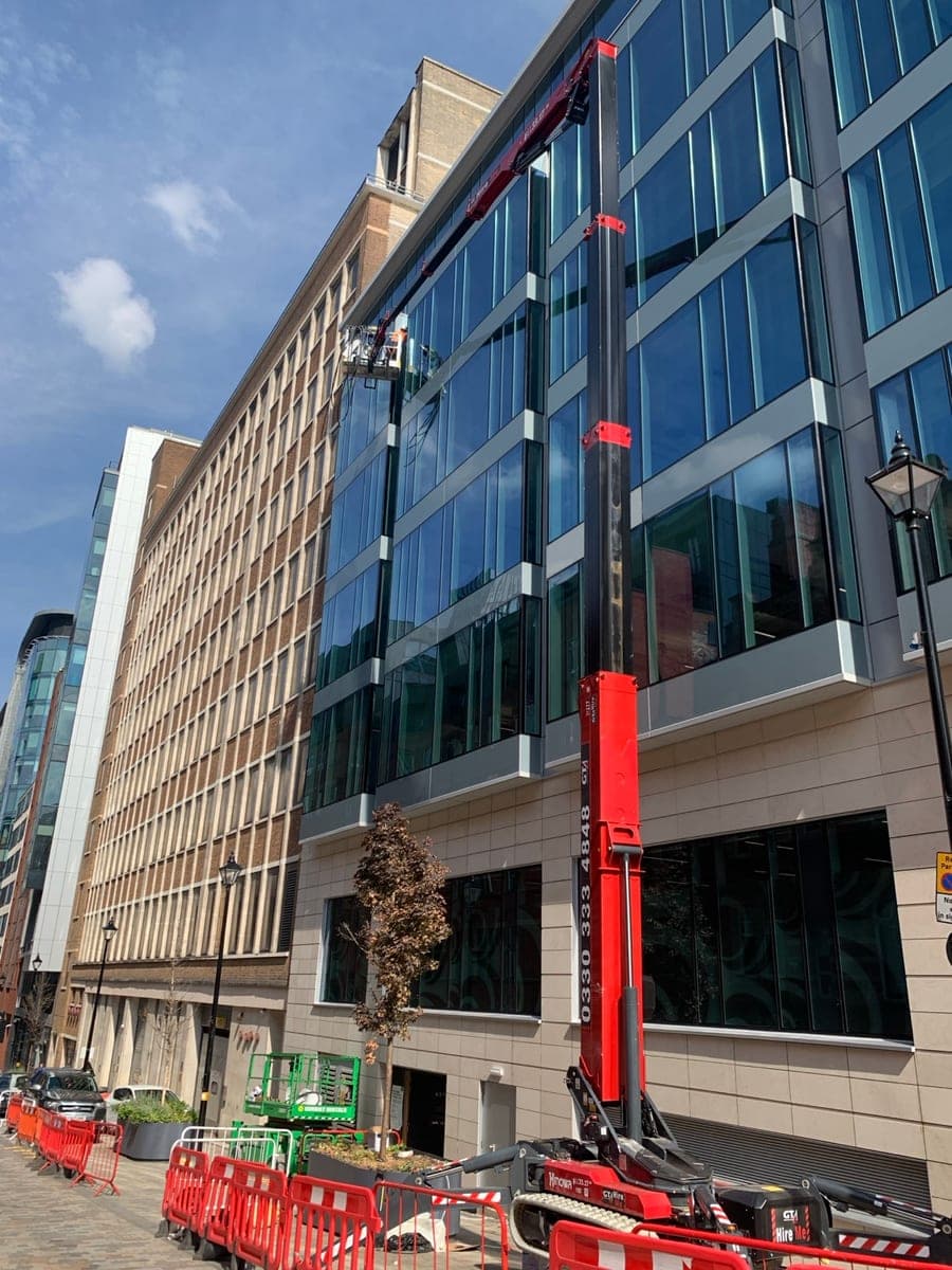 Red tracked spider lift extended up a glass-fronted office building in Birmingham city centre