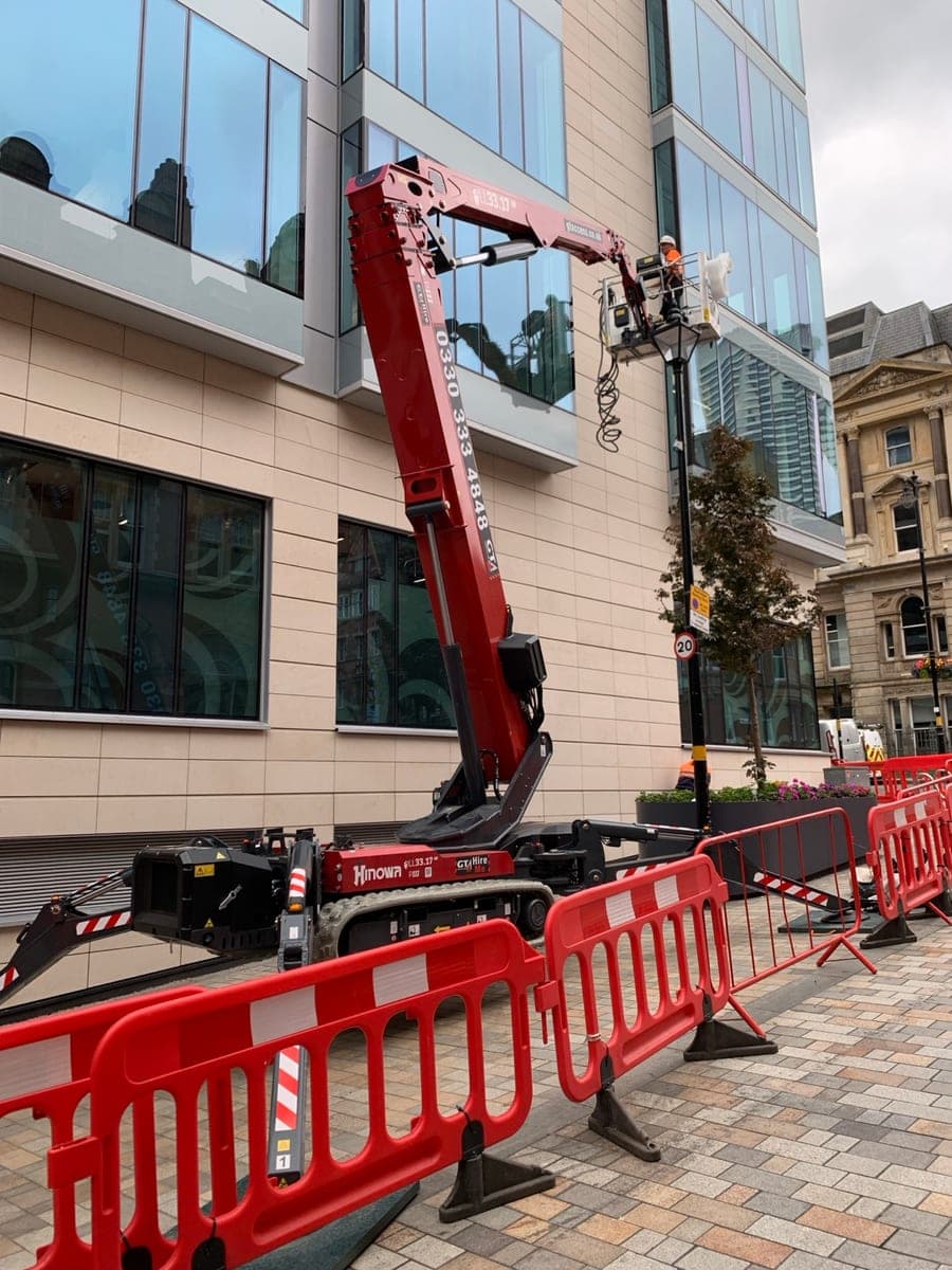 Spider lift boom fully extended with the operator platform raised beside a Birmingham building