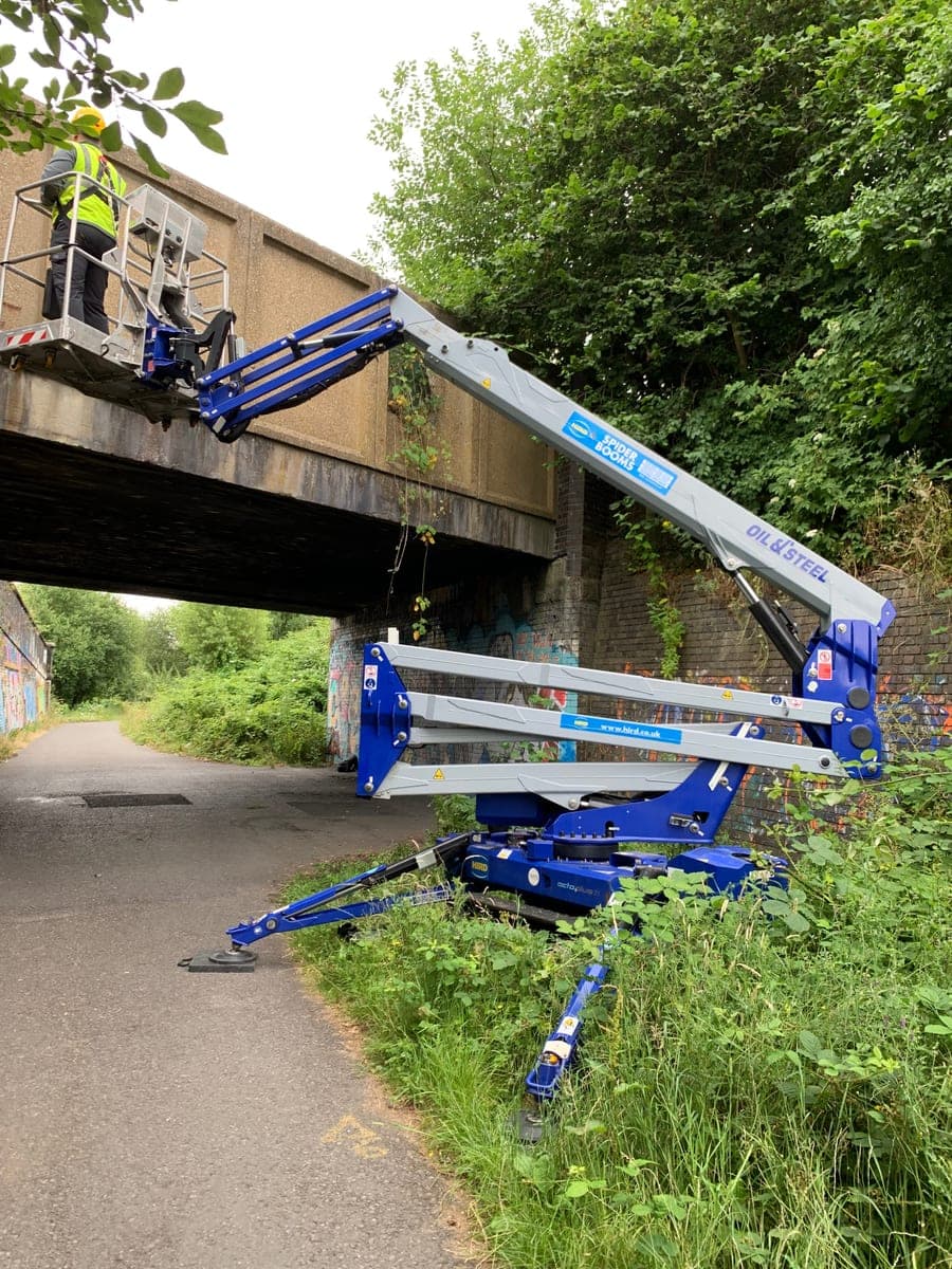Tracked spider lift with its platform raised alongside the bridge structure in Levenshulme