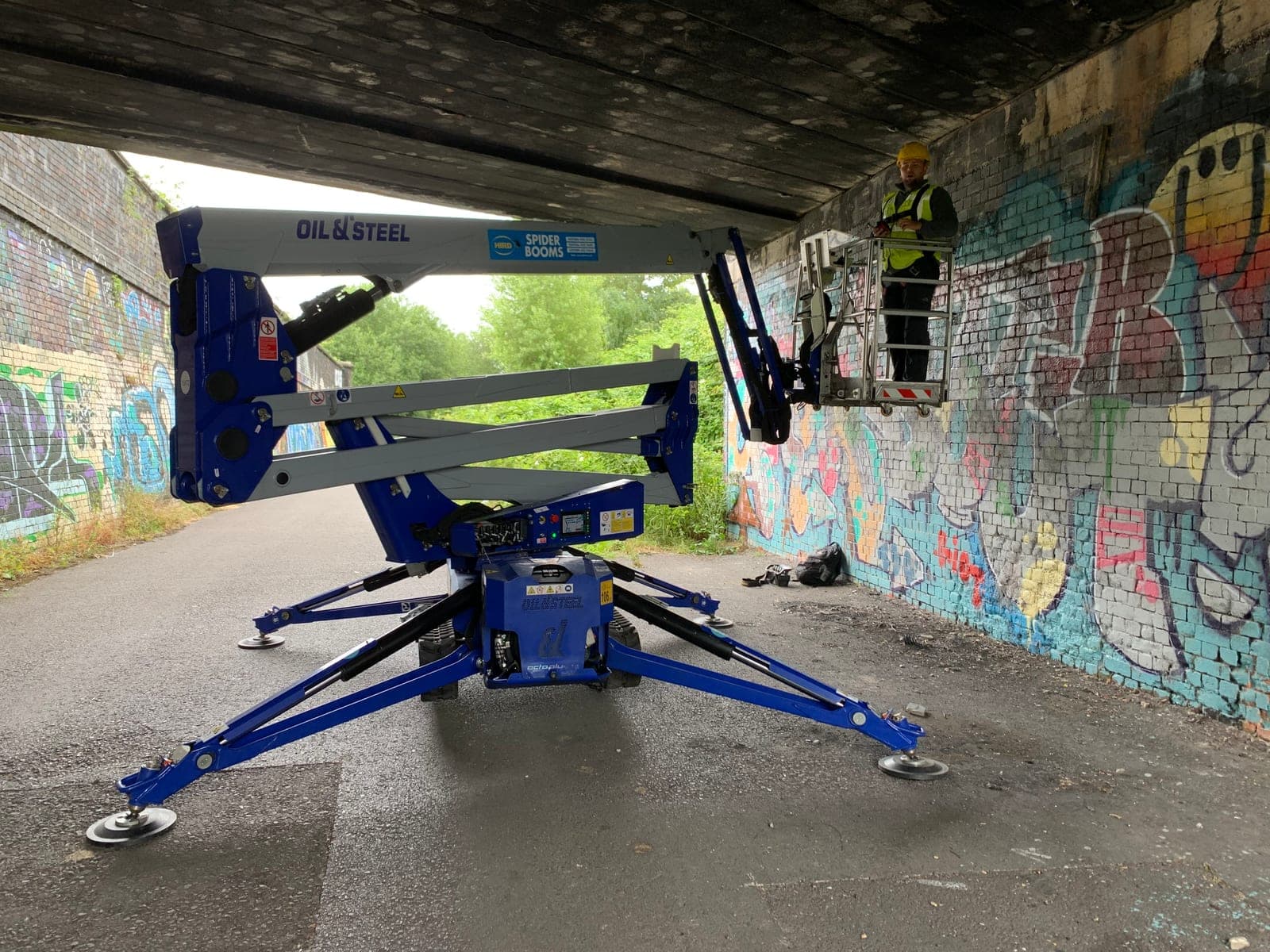Spider lift with outriggers deployed and its platform raised beneath a bridge