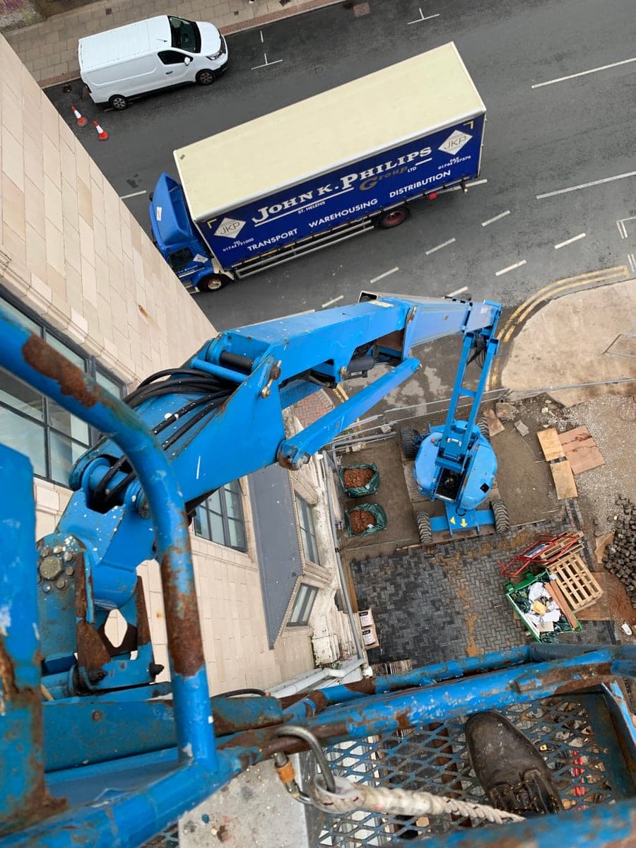 View down a blue articulated boom lift alongside a Manchester building