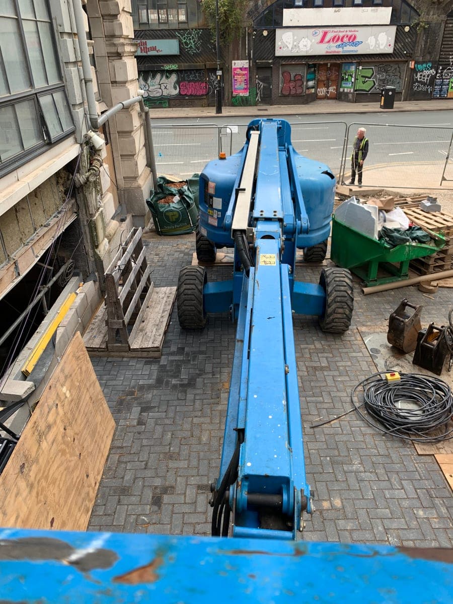 Blue boom lift beside a building in a fenced Manchester city-centre work area