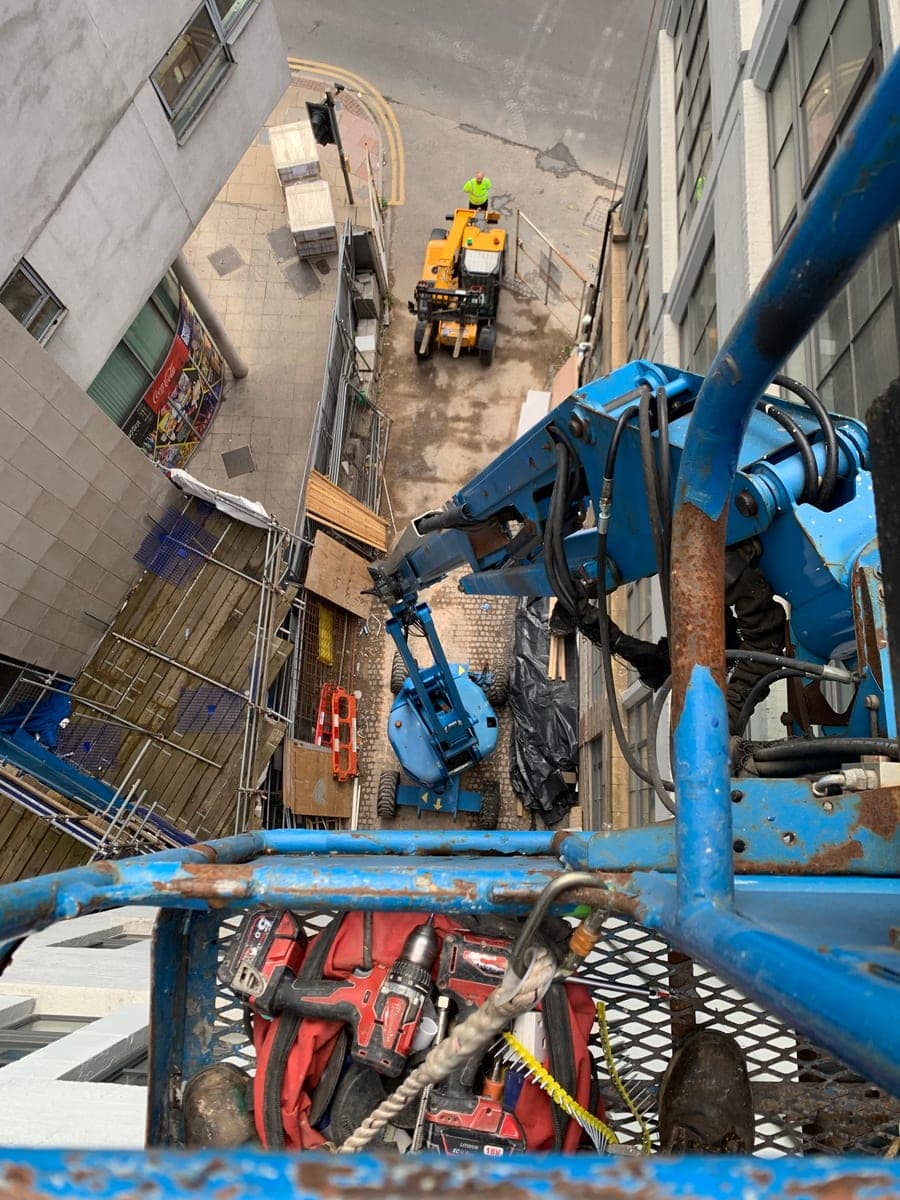 Raised cherry-picker platform beside windows above a narrow space between buildings