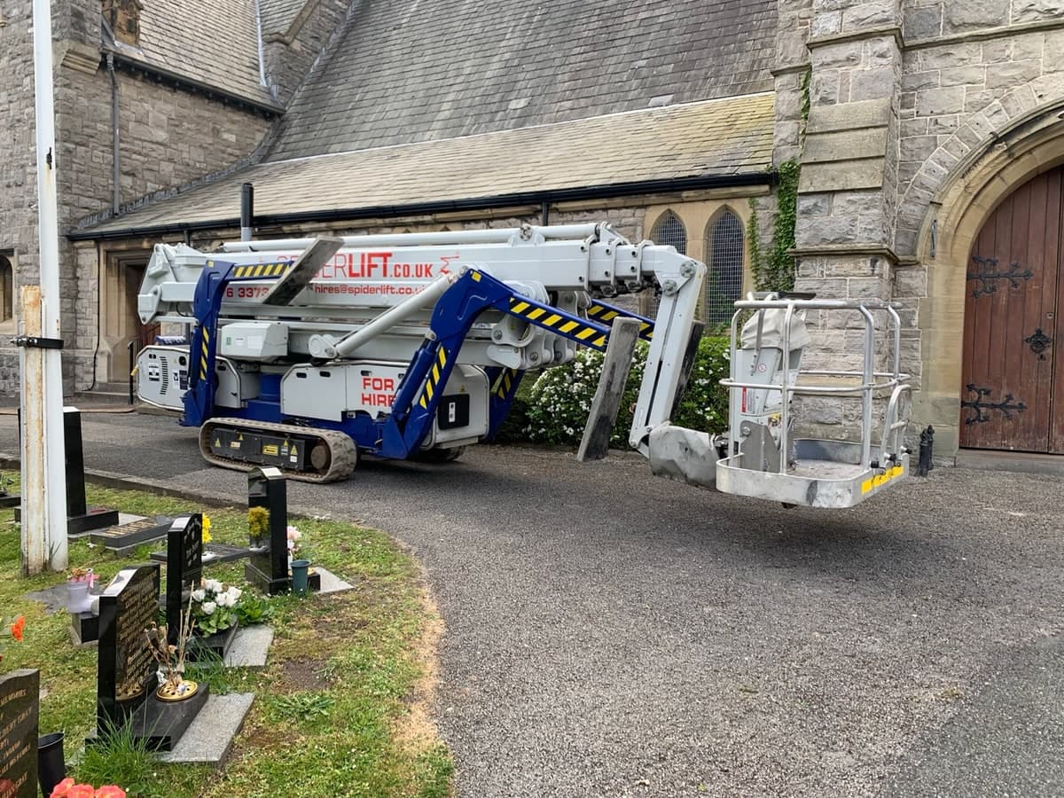 Folded tracked spider lift positioned beside a stone church in Prestatyn