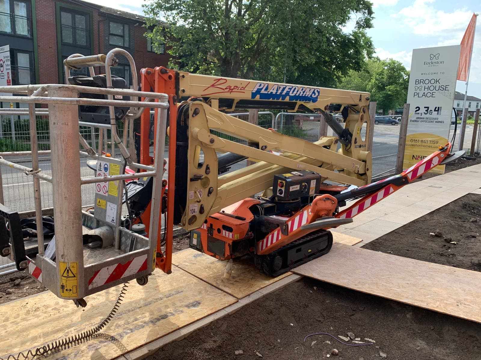 Tracked spider lift with its boom folded beside new homes in Trafford