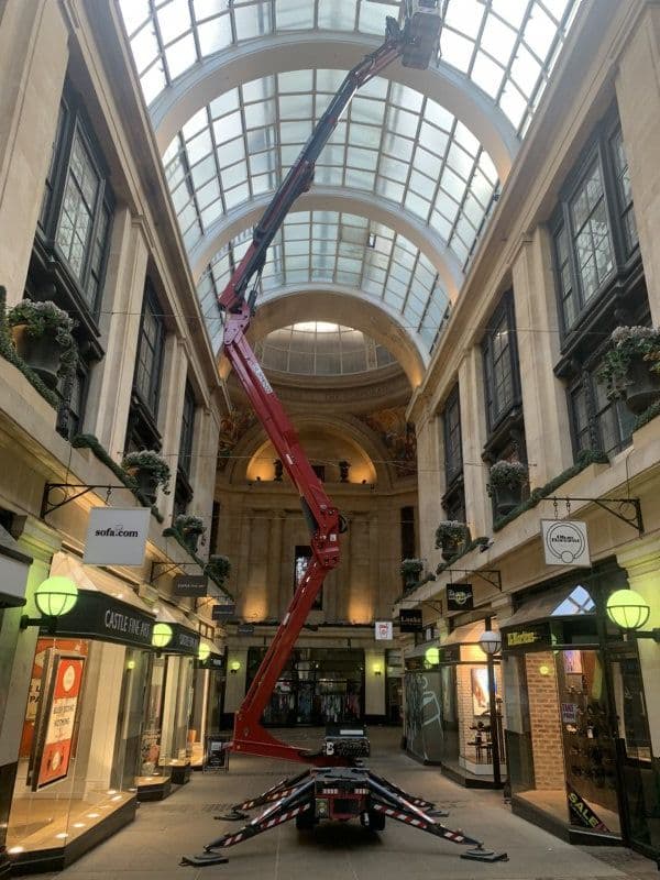 Red tracked spider lift at full height inside a Victorian shopping arcade with glass dome ceiling