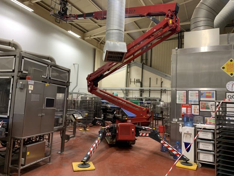 Red tracked spider lift fully deployed inside a food production facility with outriggers on the factory floor