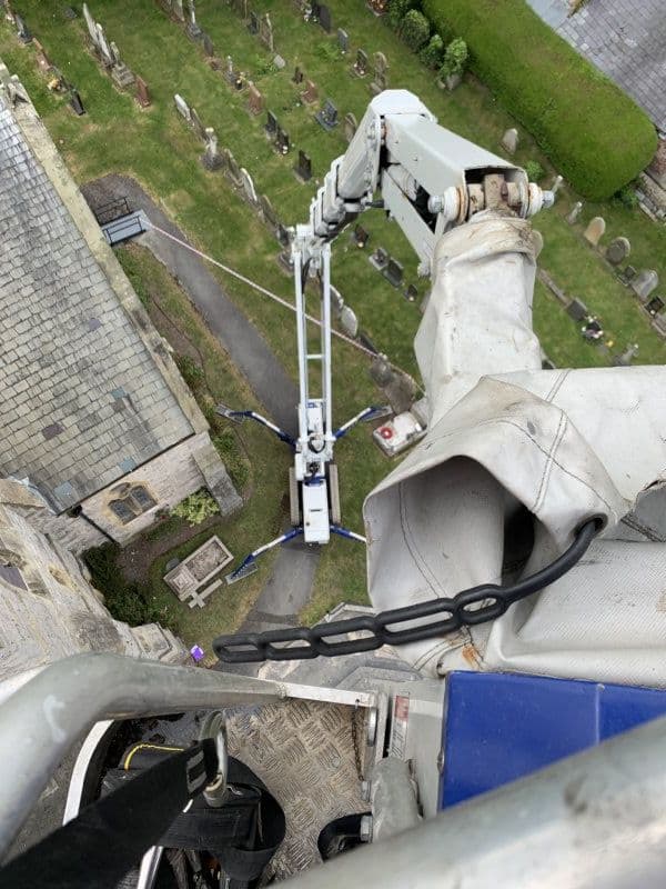 View from spider lift basket looking down at the machine outriggers deployed in a churchyard far below